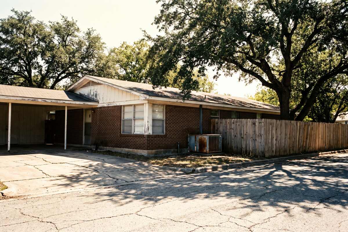 An older brick and stone ranch house in Georgetown on a wide lot under deep live oak shade.