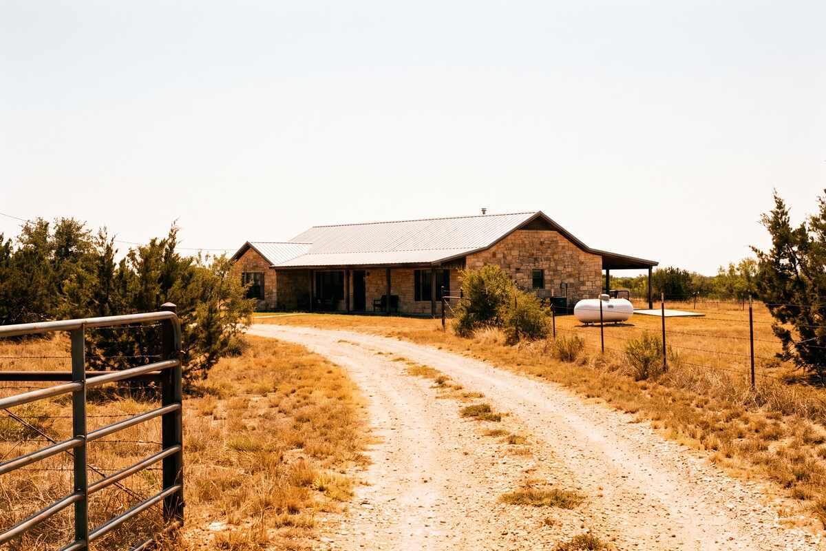 A Liberty Hill acreage home at the end of a long gravel drive with a propane tank and cedar scrub behind it.
