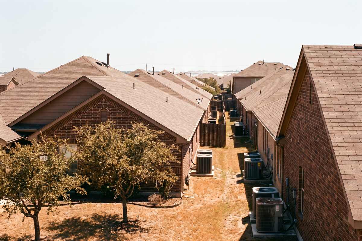 Rooftops of a dense 2000s Round Rock subdivision seen from a slight rise, outdoor condensers visible in side yards.