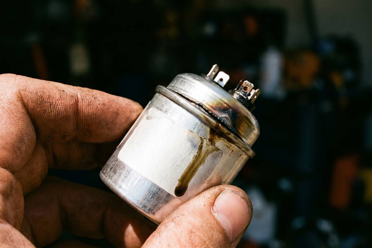 A run capacitor with a bulged and split top sitting on a truck tailgate beside its replacement.